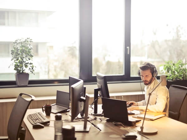 man with headphones facing computer monitor