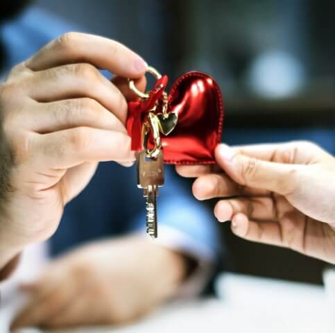 Two persons holding grey key with red heart key chain